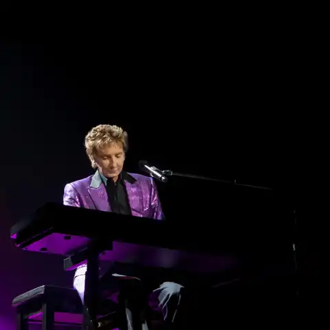 Barry Manilow performing onstage under blue and purple lighting